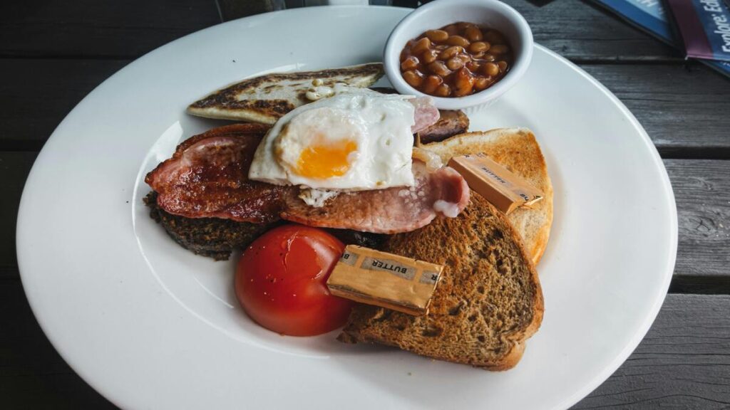 A delicious assortment of breakfast meats, including crispy bacon, sausage links, ham, and turkey bacon, served on a wooden platter with fresh herbs.