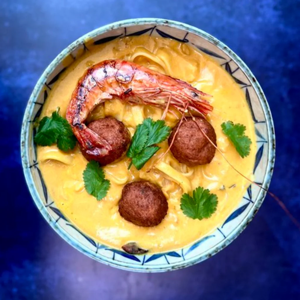 "A steaming bowl of Lava Foot and Saltric Soup from The Elder Scrolls Online, placed on a rustic wooden table with ESO-inspired ingredients around it."