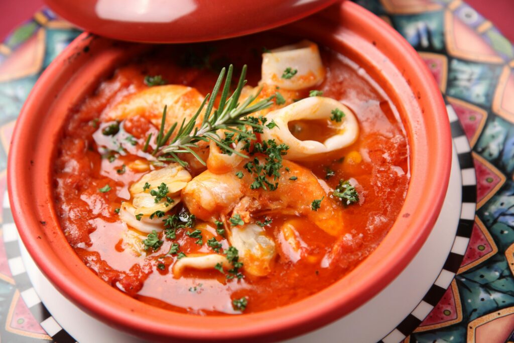 "A steaming bowl of Lava Foot and Saltric Soup from The Elder Scrolls Online, placed on a rustic wooden table with ESO-inspired ingredients around it."