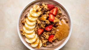 High protein yogurt bowl topped with granola, cacao nibs, and a peanut butter drizzle