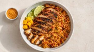 Overhead wide shot of a finished Cajun chicken and rice bowl topped with diced mango and fresh cilantro