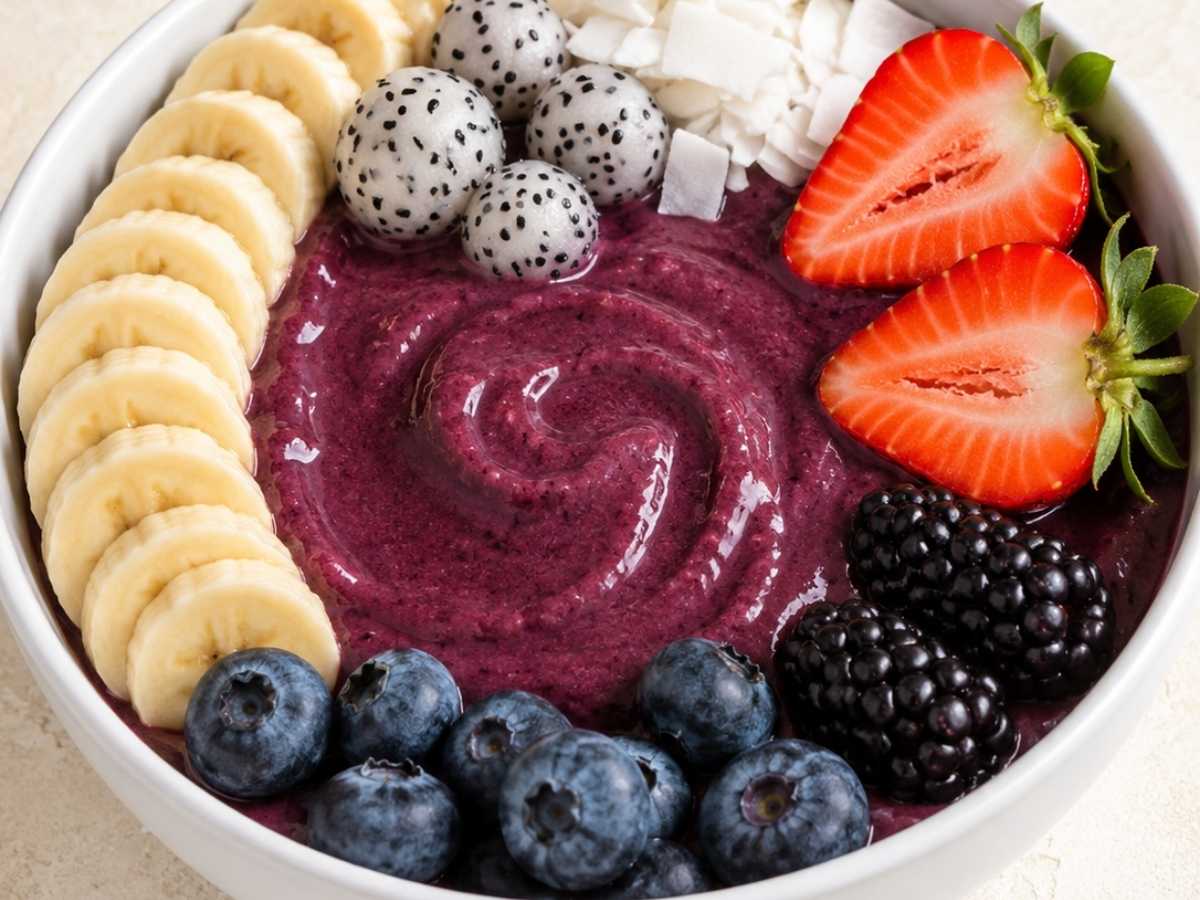 Closeup of a berry acai bowl showing the thick, creamy texture topped with sliced banana and fresh raspberries