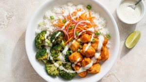 Buffalo chicken rice bowl with roasted broccoli, blue cheese, and ranch drizzle in a wide serving bowl