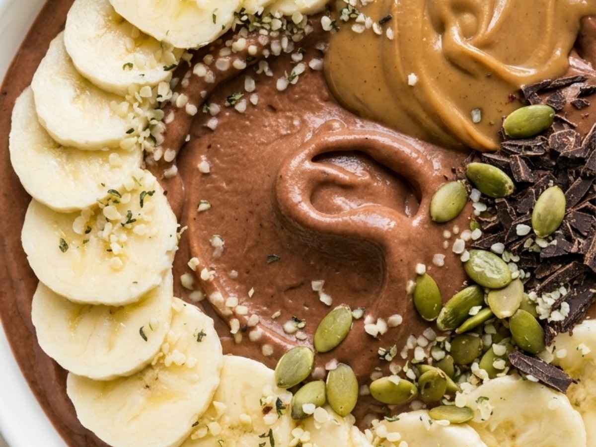 Close up of creamy chocolate smoothie bowl with a spoon resting in the thick banana base