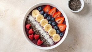Overhead wide shot of a classic acai bowl topped with sliced strawberries, banana, blueberries, raspberries, coconut, and granola