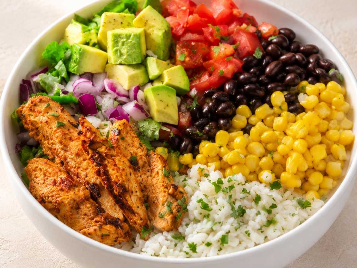 Close up of chipotle chicken, black beans, corn, and diced tomato on cilantro lime rice in a burrito bowl