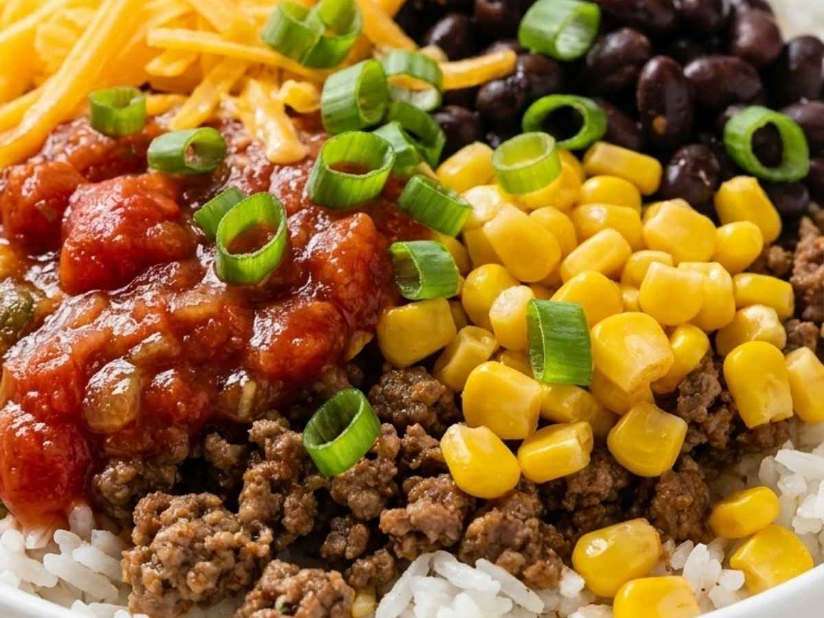 Close up of a burrito bowl layered with taco meat, black beans, corn, cheese, and salsa