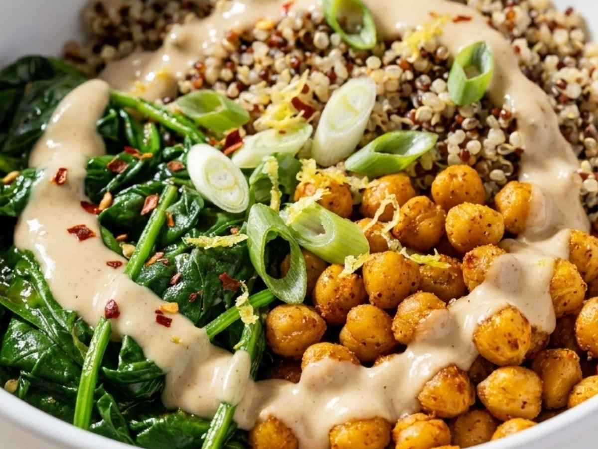 Close-up of creamy tahini chili sauce being drizzled over a quinoa bowl with roasted chickpeas and spinach