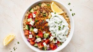 Overhead shot of a Greek chicken rice bowl with lemon rice, tzatziki, and Greek salad