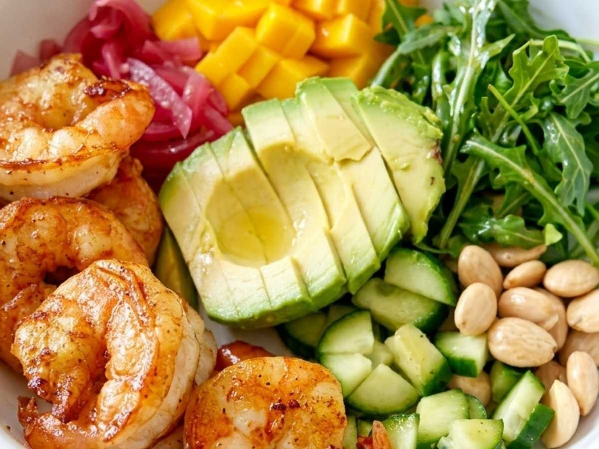 Closeup of a shrimp protein bowl showing seared shrimp, sliced avocado, and mango over arugula