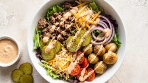 High Protein Burger Bowls with Greek Yogurt Sauce Finished high protein burger bowl with ground meat, Greek yogurt sauce, lettuce, tomato, and pickles in a wide angle shot