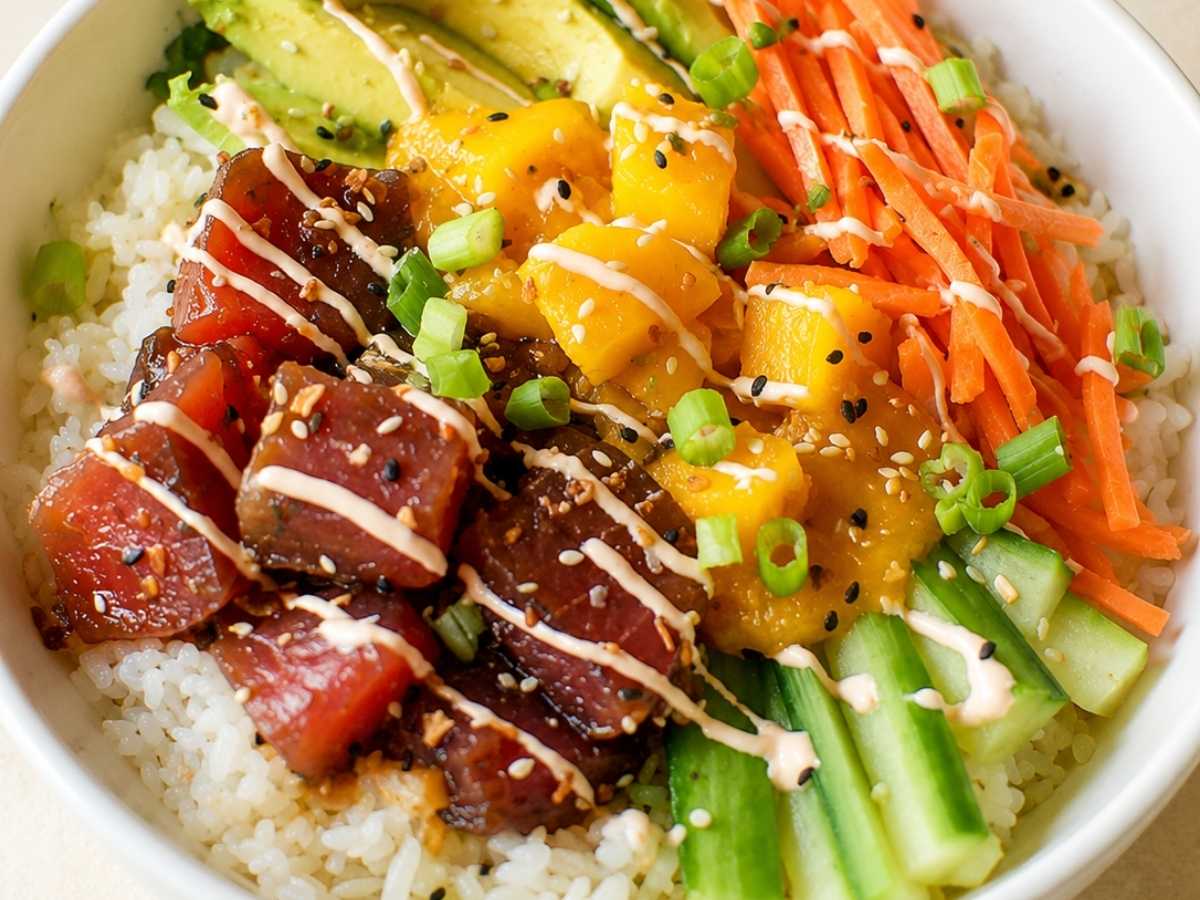 Close up of a mango poke bowl showing marinated ahi tuna, mango rum sauce, and spicy aioli drizzle