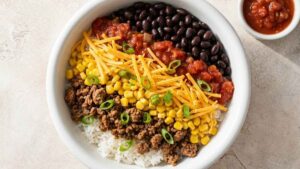 Meal Prep Burrito Bowl Four containers of meal prep burrito bowls with rice, taco meat, black beans, corn, and melted cheese