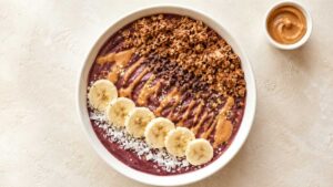 Wide angle shot of a peanut butter acai bowl topped with granola, banana slices, and a peanut butter drizzle