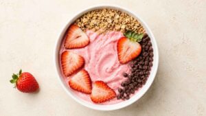 Wide angle shot of a strawberry smoothie bowl topped with sliced strawberries, granola, and chocolate chips