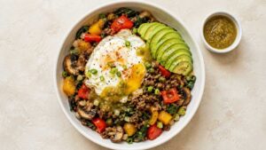 High Protein Beef Bowl Overhead wide shot of a beef protein bowl with seasoned ground beef, sauteed peppers, mushrooms, spinach, fried eggs, and avocado slices