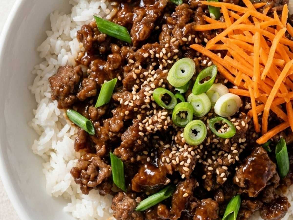 Close up of glossy Mongolian beef over rice with sesame seeds and green onion in a rice bowl