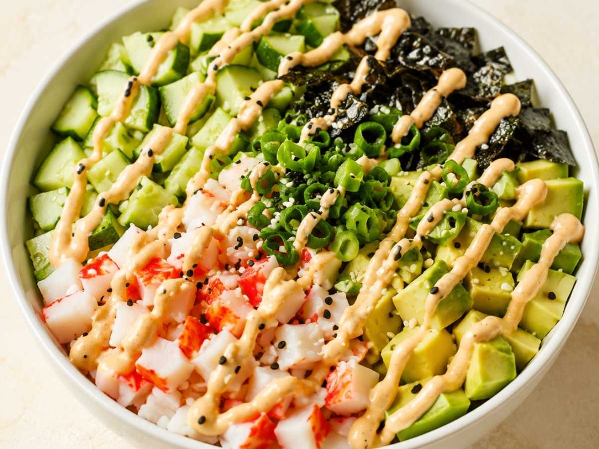 Close-up of a California roll bowl showing crab, avocado, nori strips, and sesame seeds over sushi rice