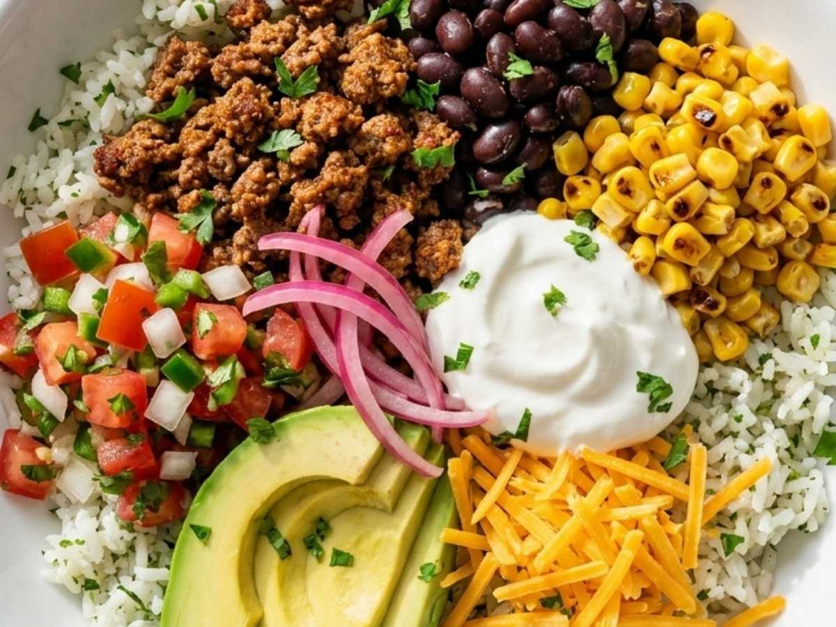 Close up of a healthy taco bowl showing avocado, pico de gallo, and shredded cheddar over seasoned beef and cilantro lime rice