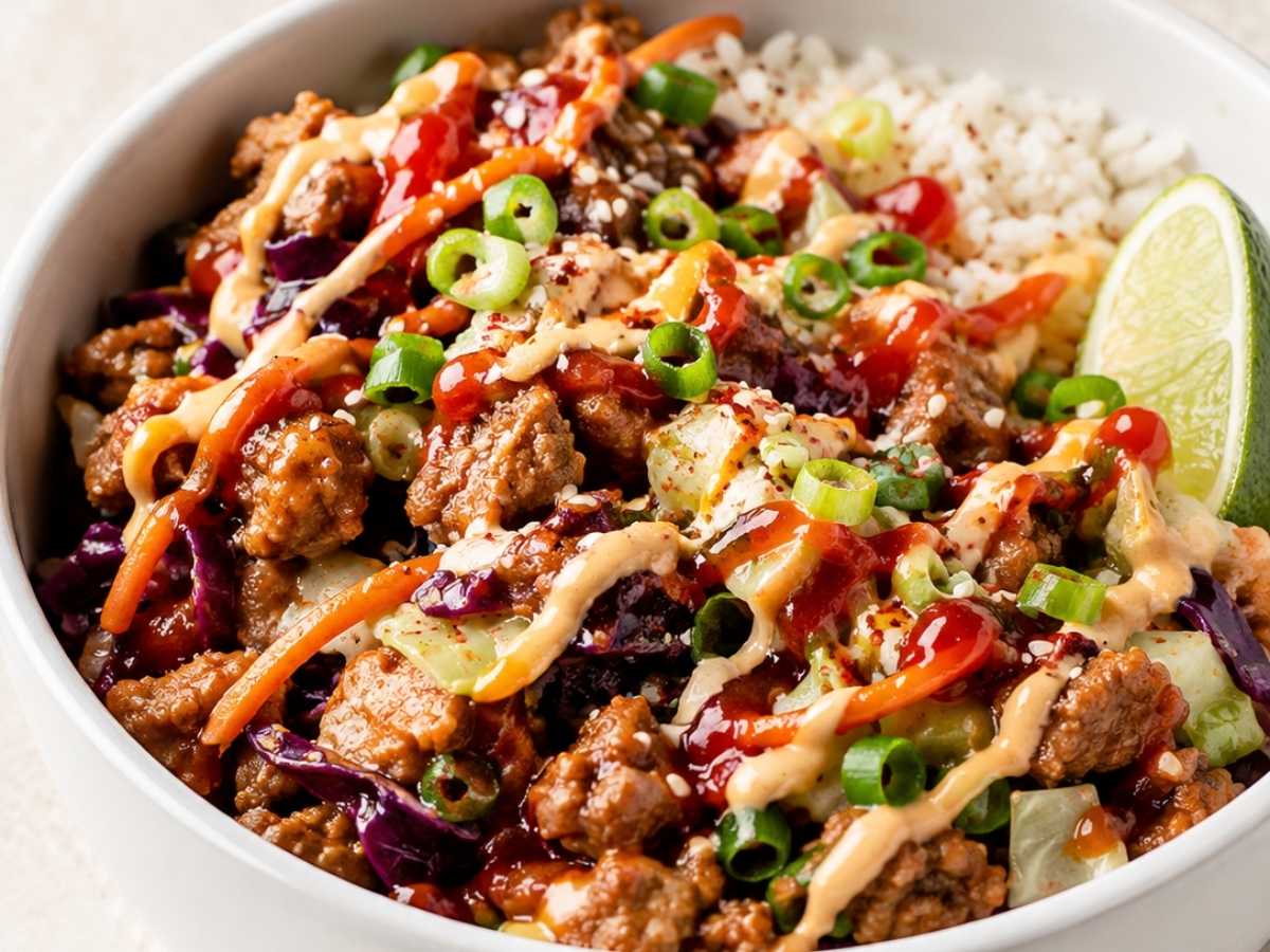 Close up of spicy egg roll in a bowl showing seared ground pork, wilted cabbage, and a creamy sriracha mayo drizzle
