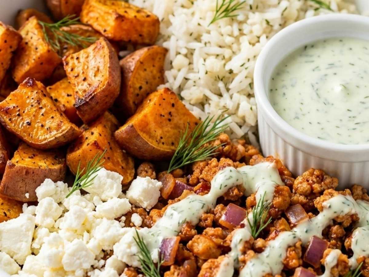 Close up of harissa ground turkey and crispy roasted sweet potatoes topped with feta yogurt sauce in a bowl