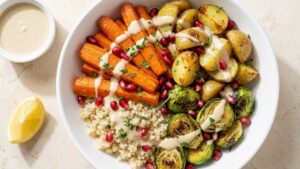 Overhead view of a harvest quinoa bowl with roasted carrots, potatoes, and Brussels sprouts, drizzled with tahini dressing