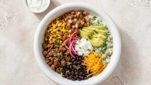Wide angle photo of a healthy taco bowl with seasoned ground beef, cilantro lime rice, black beans, charred corn, and fresh toppings