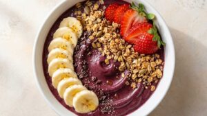High Protein Acai Bowl Wide angle shot of a high protein acai bowl topped with granola, banana slices, and fresh berries