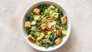 Wide angle shot of a kale Caesar salad bowl topped with croutons and shaved Parmesan