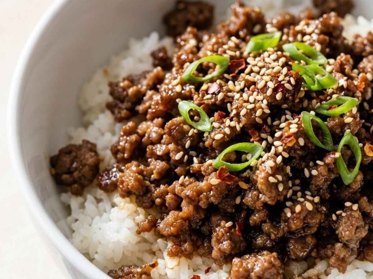 Wide overhead shot of a finished Korean beef rice bowl topped with green onions and sesame seeds.