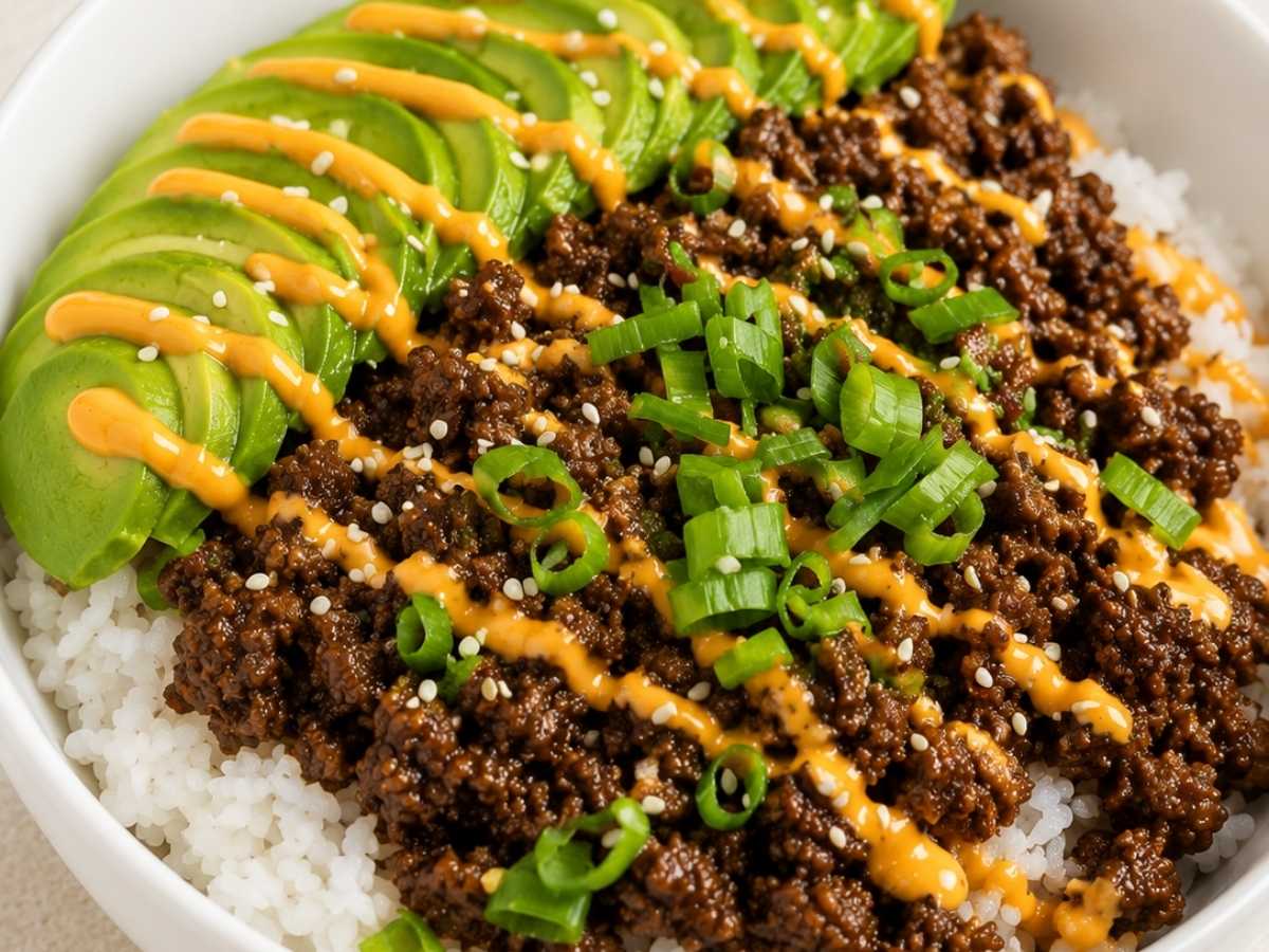 Close-up of saucy Korean-style ground beef over rice with avocado and sesame seeds