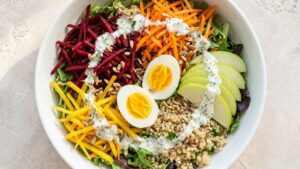 Rainbow veggie quinoa bowl topped with shredded beets, carrots, apple slices, and a halved egg