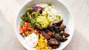 Steak Fajita Rice Bowl Overhead view of a steak fajita rice bowl with sliced steak, garlic lime rice, charred peppers and onions, and fresh toppings