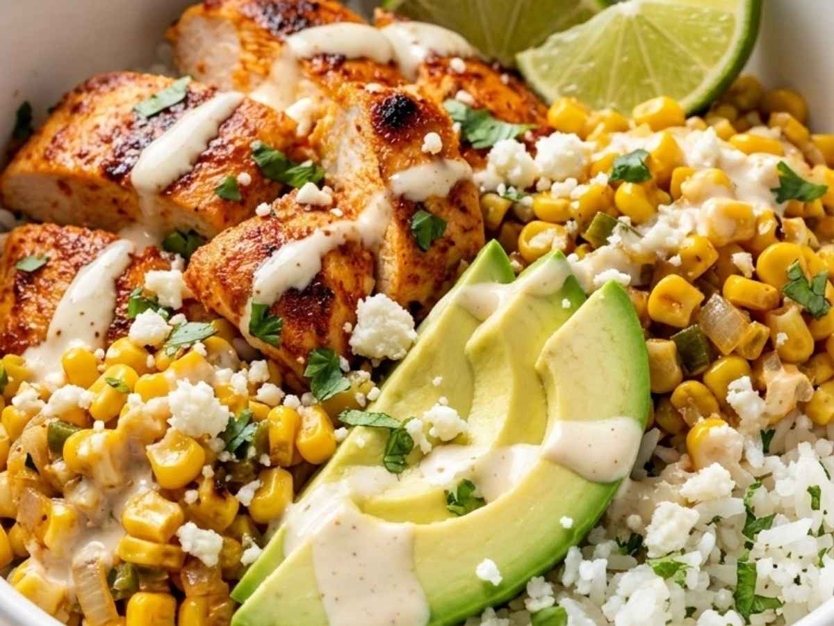 Close-up of a Street Corn Chicken Bowl showing creamy tajín sauce drizzled over charred corn, chicken, and cotija cheese