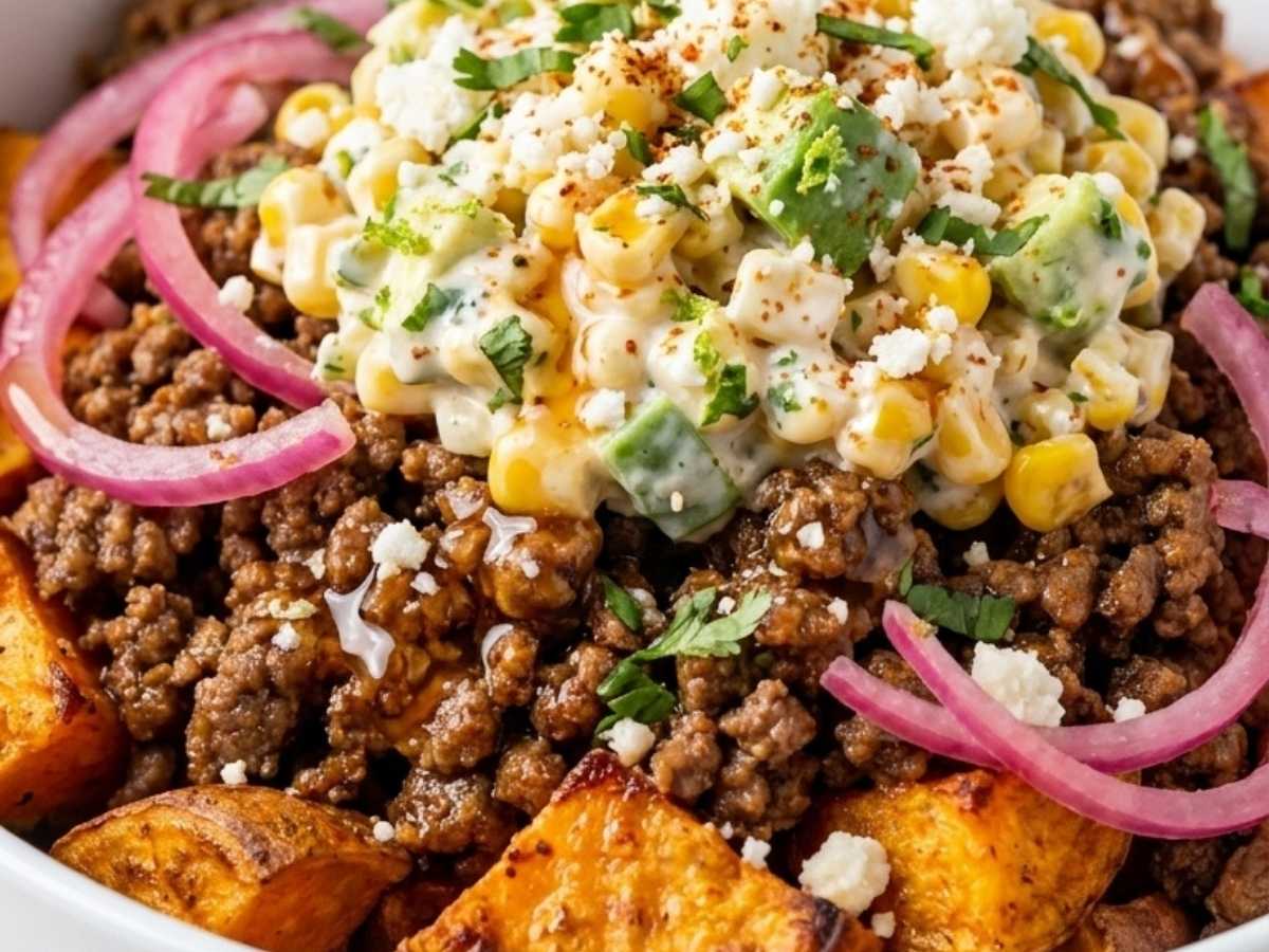Closeup of creamy street corn topping with cotija and avocado over taco beef bowl