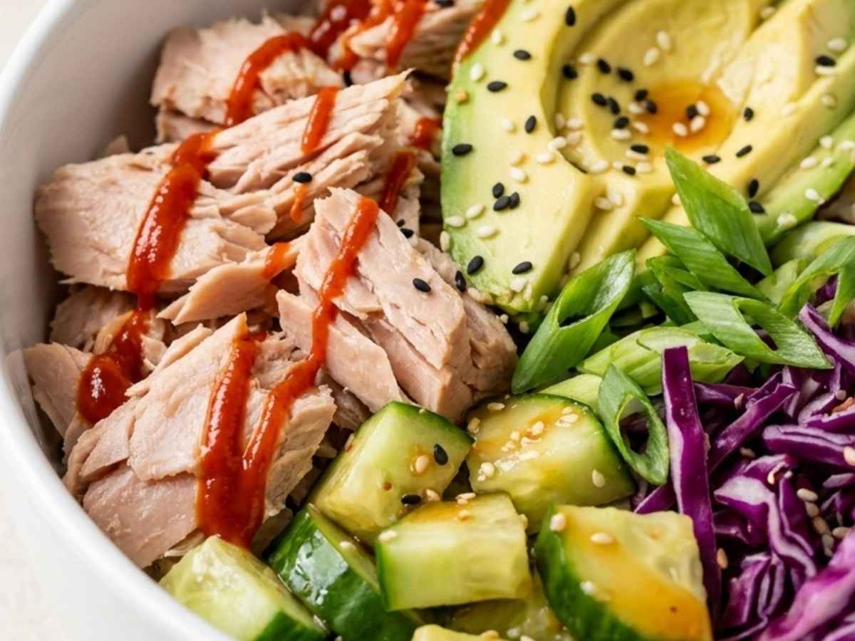 Closeup of tuna protein bowl showing avocado slices, sesame seeds, and sriracha drizzle